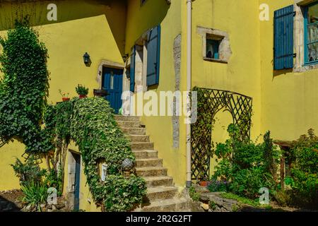 Giardino lussureggiante in una casa gialla con persiane blu a Liverdun sulla Mosella, Francia Foto Stock