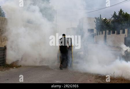 Kufr Qadoom, Nablus. 19th maggio, 2023. Un protester palestinese è visto nel fumo di barattoli di gas lacrimogeno sparati dai soldati israeliani durante gli scontri a seguito di una protesta contro l'espansione degli insediamenti ebrei nel villaggio di Kufr Qadoom, vicino a Nablus, il 19 maggio 2023. Credit: Nidal Eshtayeh/Xinhua/Alamy Live News Foto Stock