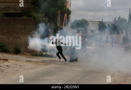 Kufr Qadoom, Nablus. 19th maggio, 2023. Un manifestante palestinese corre per prendere copertura da un barattolo di gas lacrimogeno sparato da un soldato israeliano durante gli scontri a seguito di una protesta contro l'espansione degli insediamenti ebrei nel villaggio di Kufr Qadoom, vicino a Nablus, il 19 maggio 2023. Credit: Nidal Eshtayeh/Xinhua/Alamy Live News Foto Stock