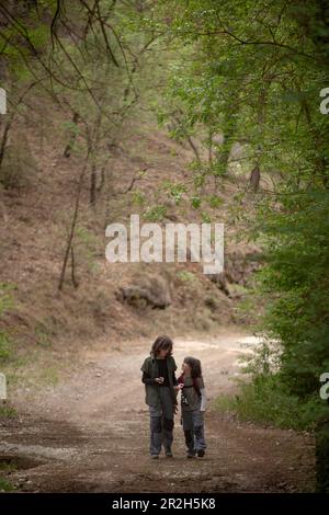 Due bambini camminano lungo un sentiero nella foresta, immersi nella conversazione mentre esplorano la bellezza della natura, favorendo la connessione e le esperienze condivise. Foto Stock