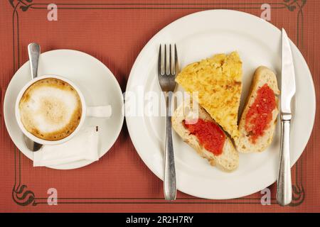 Una tipica colazione spagnola con spiedino di tortilla con fette di pane con pomodoro e caffè con latte in una tazza Foto Stock