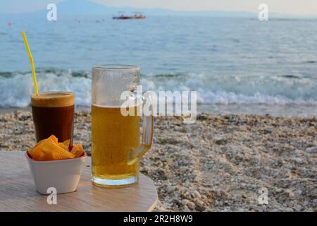 Snack e bevande al mare, caffè freddo frappe, birra ghiacciata e patatine nel tardo pomeriggio, Pefkari spiaggia, isola di Thassos, Grecia Foto Stock