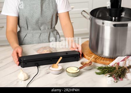 Donna che usa il sigillante per il confezionamento sottovuoto in cucina, closeup. Cucina sous vide Foto Stock