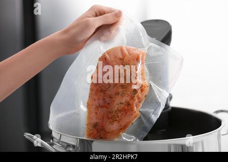 Donna che mette la carne sottovuoto impaccata in pentola con cucina sous vide, primo piano. Circolatore a immersione termica Foto Stock