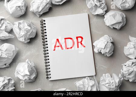 Soluzione alternativa delle controversie. Notebook con abbreviazione ADR circondato da palline di carta su tavolo grigio chiaro, piatto Foto Stock