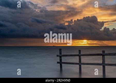 Tramonto sul mare. recinzione di legno nell'acqua. Il sole si spegne da dietro le nuvole. Lolland, Danimarca, Fehmarn Belt Foto Stock