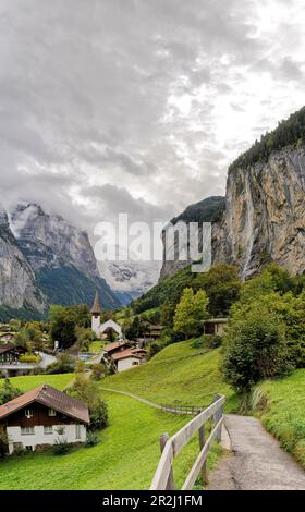 Percorso tra prati verdi del villaggio alpino di Lauterbrunnen con cascate Trummelbach sullo sfondo, Cantone di Berna, Svizzera, Europa Foto Stock