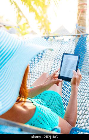 Donna allegra su un'amaca che ama leggere un libro digitale su tablet, Zanzibar, Tanzania, Africa orientale, Africa Foto Stock