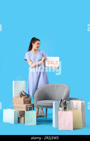 Venditore femminile con segno di vendita, scatole di scarpe, borse per la spesa e poltrona su sfondo blu Foto Stock