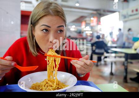 Giovane donna che mangia presso la tradizionale bancarella di cibo Asiatico nel centro dei falchi del Singapore Food Trail, Singapore, Asia sudorientale Foto Stock