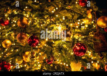 Baubles in rosso e oro che scintillano sull'albero di Natale con luci fata Foto Stock