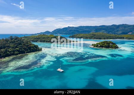 Vista aerea di un catamarano a vela in acque turchesi limpide con isole dietro, St Anne Marine National Park, vicino a Mahé Island, Seychelles, Indian O. Foto Stock