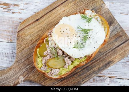 Toast all'avocado con tonno, uova fritte e aneto sul tagliere. Foto Stock