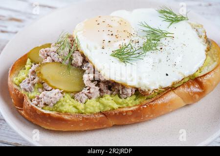 Toast all'avocado con tonno, uova fritte e aneto sul piatto. Foto Stock