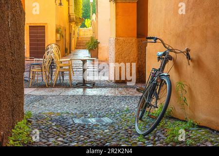 Strada acciottolata medievale con biciclette e palazzi gialli nella città di Verona, Veneto, Italia, vuota strada italiana nel centro storico. Destinazione di viaggio Foto Stock