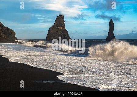 Onde oceaniche possenti che si infrangono contro le pile di basalto mare di Reynisdrangar e sulla sabbia nera della spiaggia di Reynisfjara, vicino a Vík í Mýrdal, Islanda Foto Stock