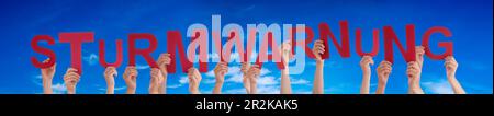 Persone mani costruire parola Sturmwarnung significa Storm Warning, cielo blu Foto Stock
