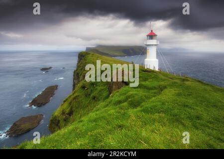 Vista delle scogliere e del faro di Mykines Holmur fino a Mykines, Isole Faeroe. Nuvole scure. Foto Stock