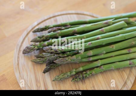 Tiri di asparagi verdi su un tagliere e un tavolo di legno, verdure deliziose in primavera, spazio copia, fuoco selezionato, profondità di campo ristretta Foto Stock