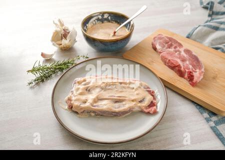 La bistecca di maiale crudo è rivestita con una marinata di yogurt con ingredienti come erbe, spezie, olio e aglio per rendere la carne succosa e morbida quando frigge, selec Foto Stock