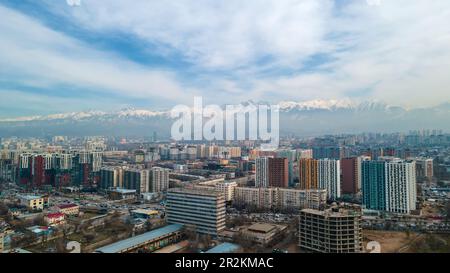 Almaty, Kazakhstan - Mart 11, 2023: Area urbana con nuovi alti edifici. Sullo sfondo di montagne e cielo nuvoloso. Foto Stock