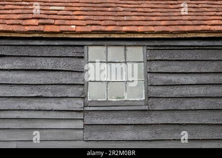 Legno nero, tetto piastrellato, fienile Sussex con finestra quadrata con nove pannelli finestra quadrata primo piano dettaglio che forma il disegno astratto Foto Stock