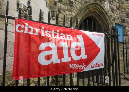 Christian Aid Week è qui banner fuori dall'ingresso della chiesa di Santa Maria Vergine, Mortlake High Street, Mortlake, Londra, SW14, Inghilterra, Regno Unito Foto Stock