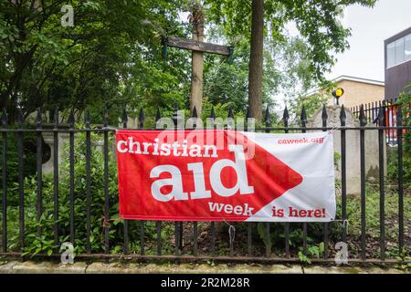 Christian Aid Week è qui banner al di fuori della chiesa di St Mary the Virgin, Mortlake High Street, Mortlake, Londra, SW14, Inghilterra, Regno Unito Foto Stock