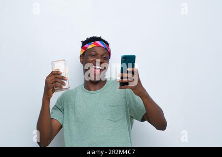 felice giovane uomo africano in possesso di contanti e utilizzando il suo telefono Foto Stock
