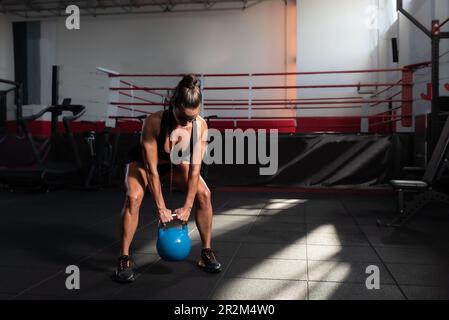 Giovane atleta sudata muscolare attiva donna pesante kettlebell allenamento crossfit allenamento hardcore in palestra. Forte esercizio femminile per streng resistenza Foto Stock