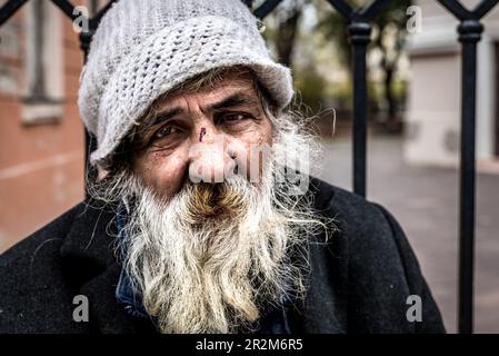 Primo piano ritratto di vecchio uomo senza tetto alcolico volto con barba bianca e capelli vagando per la strada depresso malato e solitario, problemi sociali di casa Foto Stock