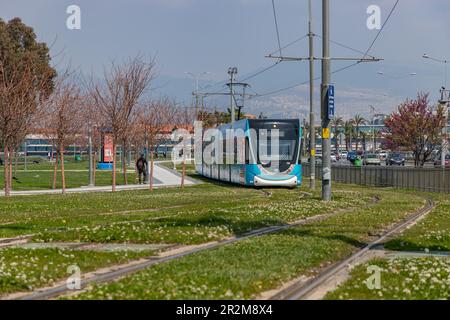 Un'immagine di un tram blu a Izmir cavalcando su piste con erba verde. Foto Stock