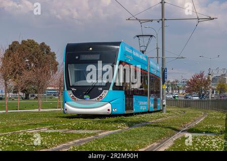 Un'immagine di un tram blu a Izmir cavalcando su piste con erba verde. Foto Stock