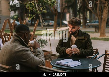 Due colleghi di affari multirazziali che hanno conversazione seria circa il progetto mentre prendono il loro primo caffè di mattina Foto Stock