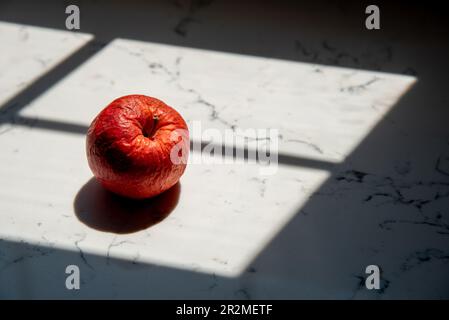 Mela rossa secca marcio malsana su un tavolo. Frutta malsana e non igienica Foto Stock