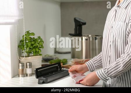 Donna che usa il sigillante per il confezionamento sottovuoto in cucina, closeup. Cucina sous vide Foto Stock