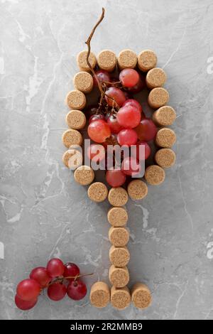 Bicchiere di vino fatto con tappi in bottiglia e uva su tavola grigia, piatto Foto Stock