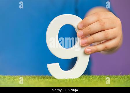 Numero 9 in mano. Una mano tiene un numero bianco nove su uno sfondo viola, nove per cento all'anno. Banner pubblicitario o biglietto d'auguri. Concetto per Foto Stock