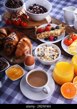 Colazione servita con caffè, succo d'arancia, croissant, pancake, uova, cereali e frutta Foto Stock