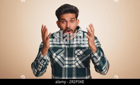 OH mio Dio, Wow. Eccitato stupito vincitore uomo alzando le mani in sorpresa guardando la telecamera con gli occhi grandi, scioccato da improvvisa vittoria. Sincero bel ragazzo indiano isolato da solo su sfondo beige studio Foto Stock