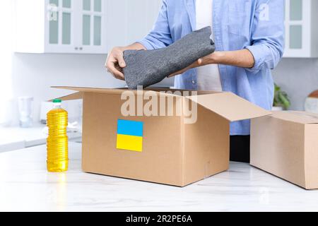 Aiuto umanitario a favore dell'Ucraina. Uomo che mette i vestiti nella scatola di donazione al tavolo bianco all'interno, primo piano Foto Stock