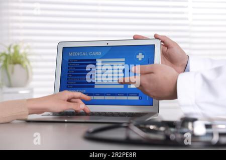 Medico e paziente che usano il portatile per compilare la scheda medica a tavolo in clinica, primo piano Foto Stock