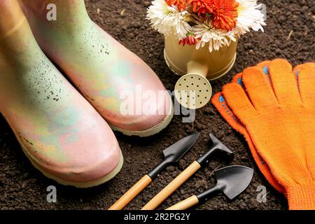 Attrezzi da giardinaggio, guanti, stivali e fiori su terreno fresco Foto Stock