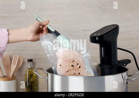 Donna che mette la carne sottovuoto impaccata in pentola con cucina sous vide, primo piano. Circolatore a immersione termica Foto Stock