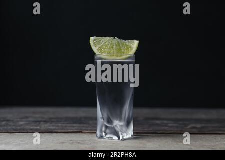 Colpo di vodka con fettina di lime su tavolo di legno Foto Stock