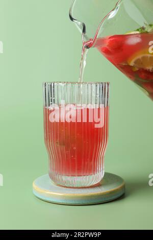Versare una gustosa bevanda estiva di cocomero con il lime della caraffa nel bicchiere su sfondo verde chiaro Foto Stock