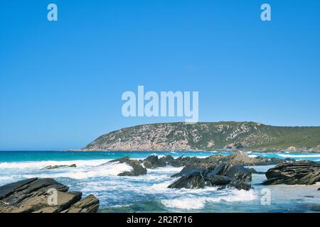 Onde che si infrangono su rocce taglienti, con un promontorio roccioso sullo sfondo, in una giornata di sole. West Beach, Fitzgerald River National Park, Australia Occidentale Foto Stock