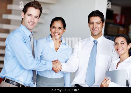 Heres ad una collaborazione riuscita. Due uomini d'affari che sigilla l'accordo con una stretta di mano mentre i loro colleghi guardano felicemente. Foto Stock