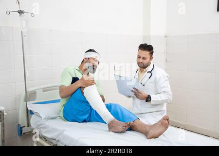 Paziente indiano con frattura ossea che ascolta, giovane uomo ferito con gamba rotta che parla con traumatologo o chirurgo ortopedico durante l'esame medico Foto Stock