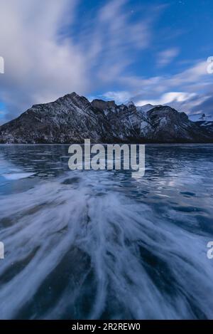 Modelli nel ghiaccio del lago Minnewanka con il Monte Inglismaldie nel Parco Nazionale di Banff sullo sfondo al crepuscolo Foto Stock